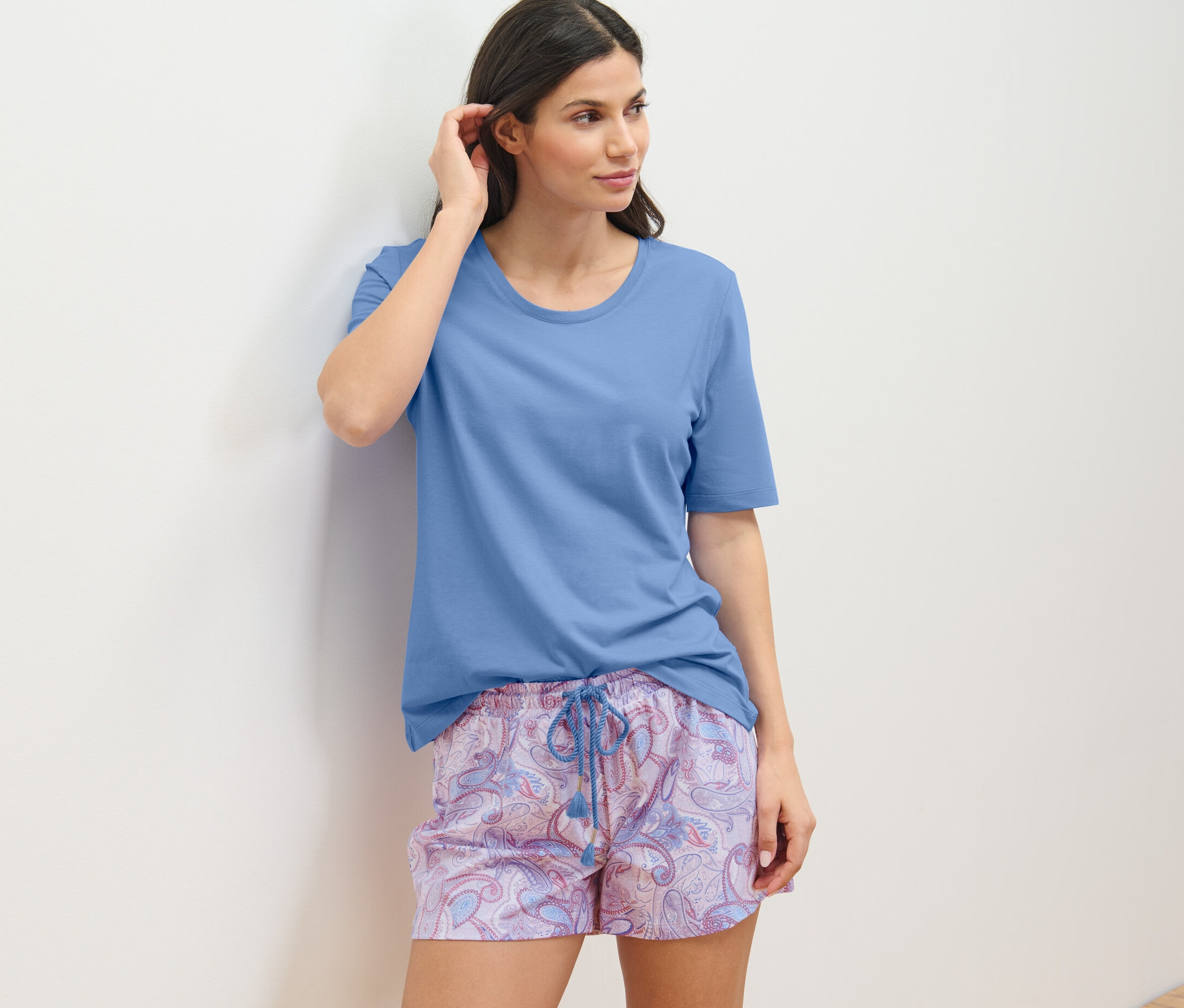 Žena v krátkej pyžamovej súprave sa opiera o stenu.