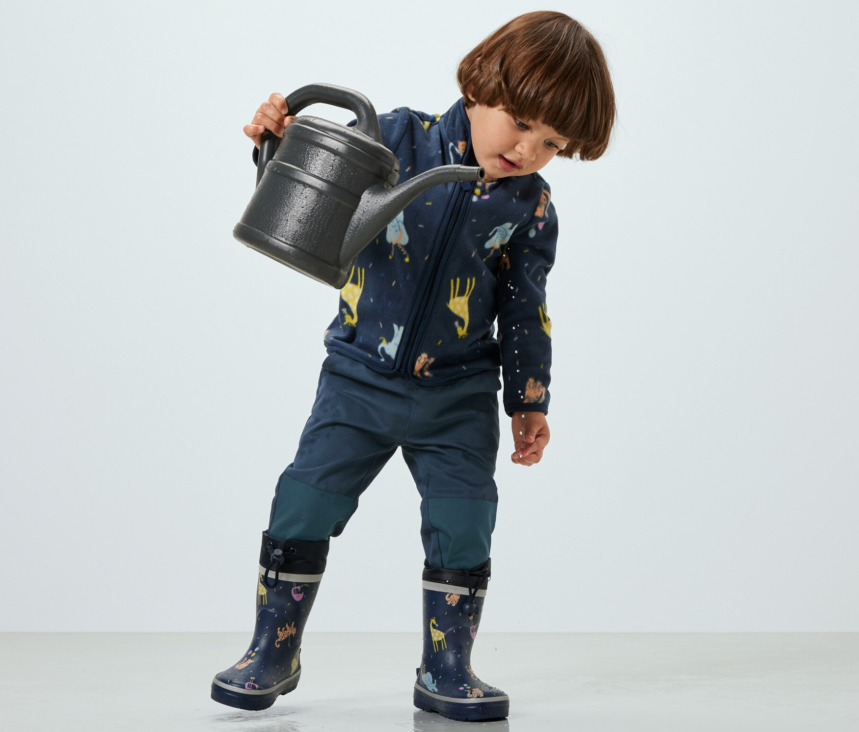 Dieťa drží kanvicu a má na sebe detské outdoorové nohavice.