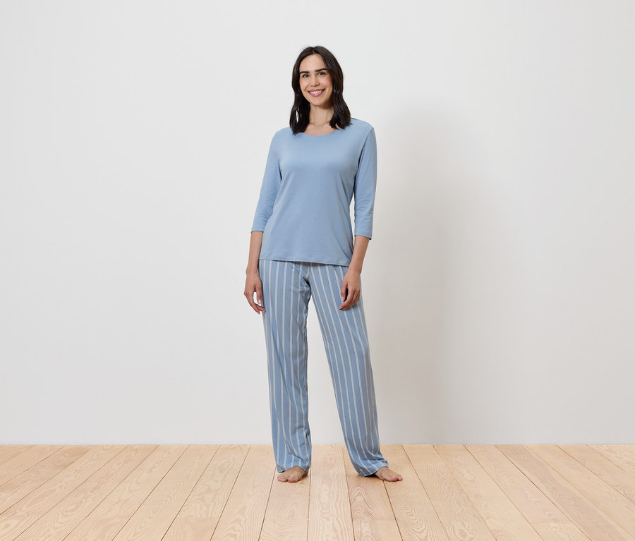 Žena stojí a má na sebe modré pruhované pyžamo.