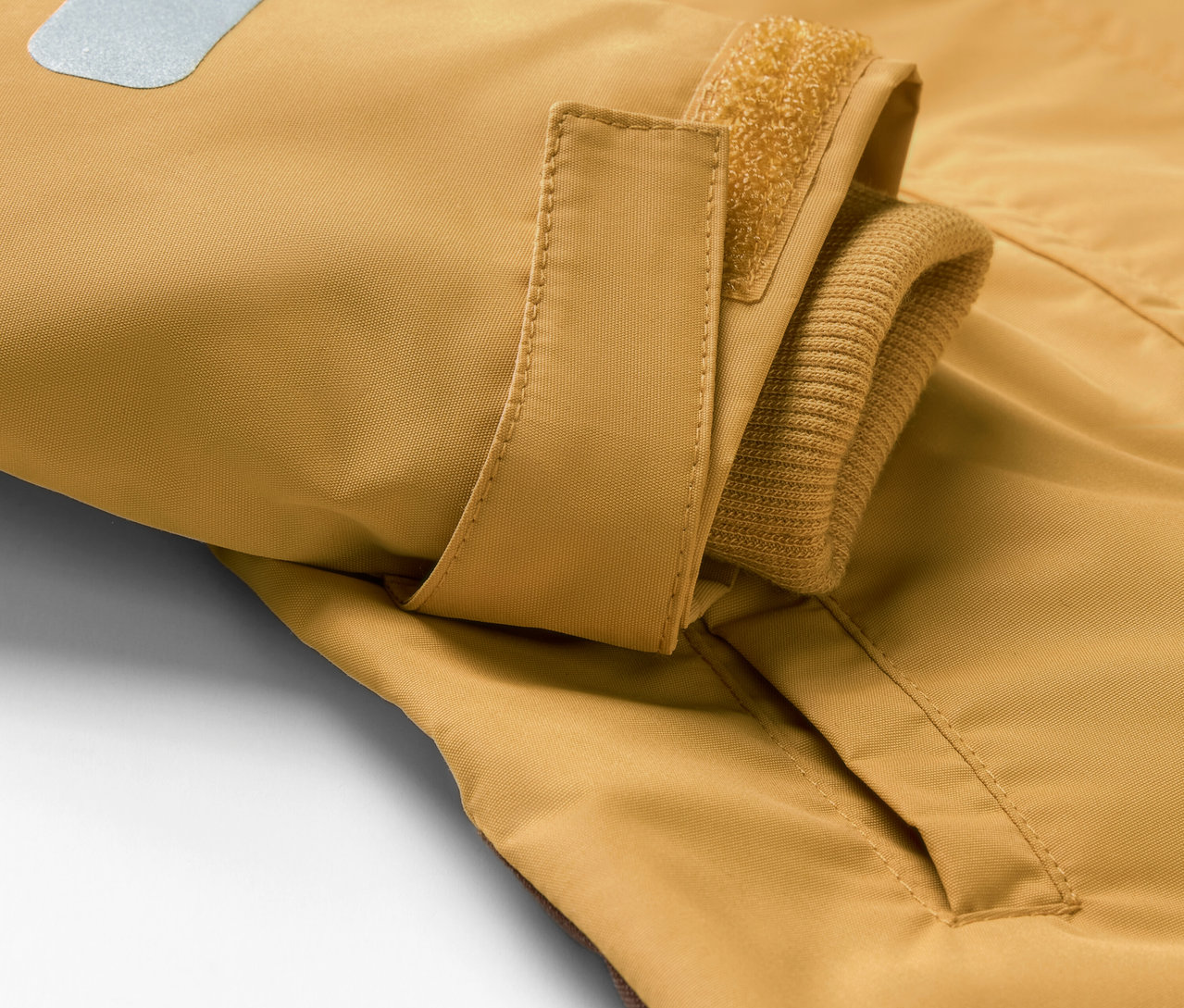 Detail detskej kombinézy do dažďa s vreckom a reflexným prvkom.