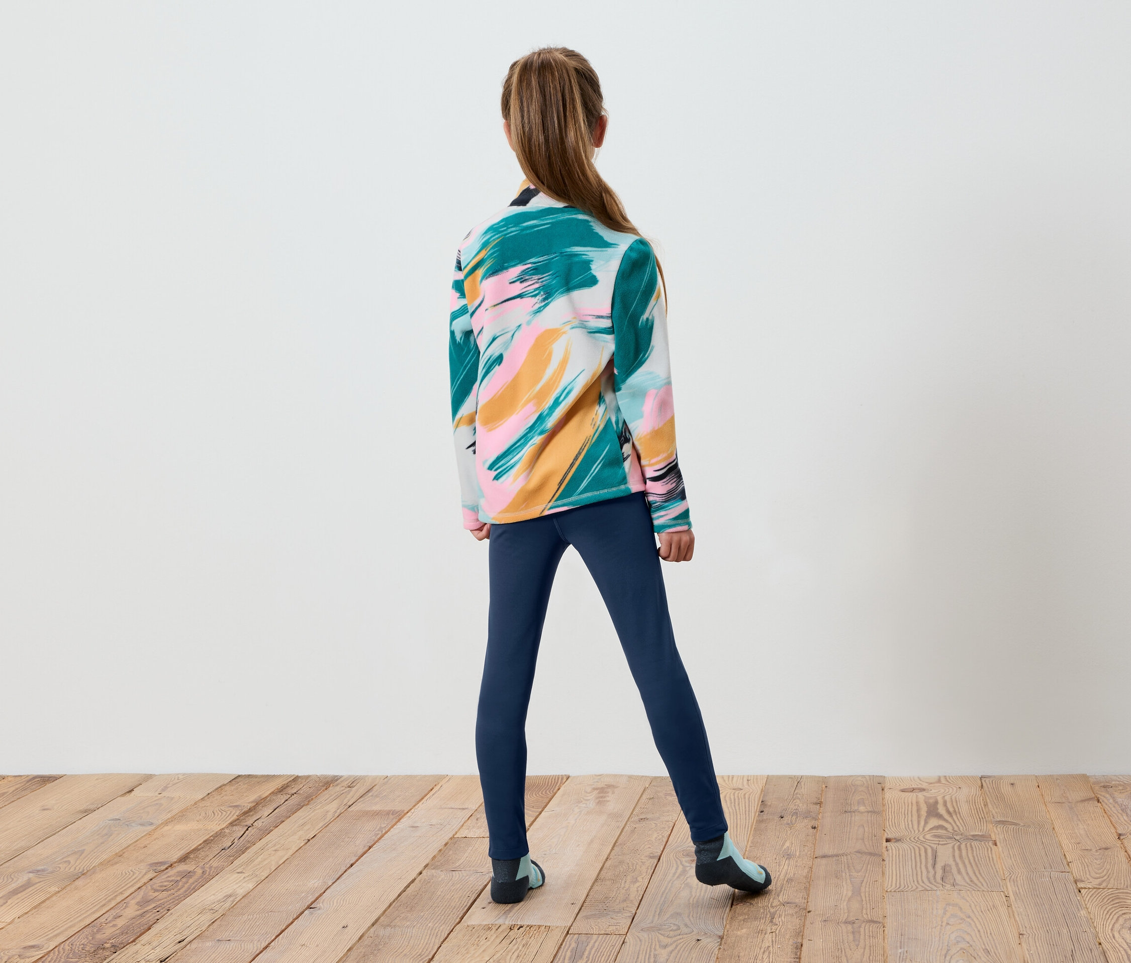 Dievča stojí chrbtom, má na sebe farebný sveter a modré legíny.