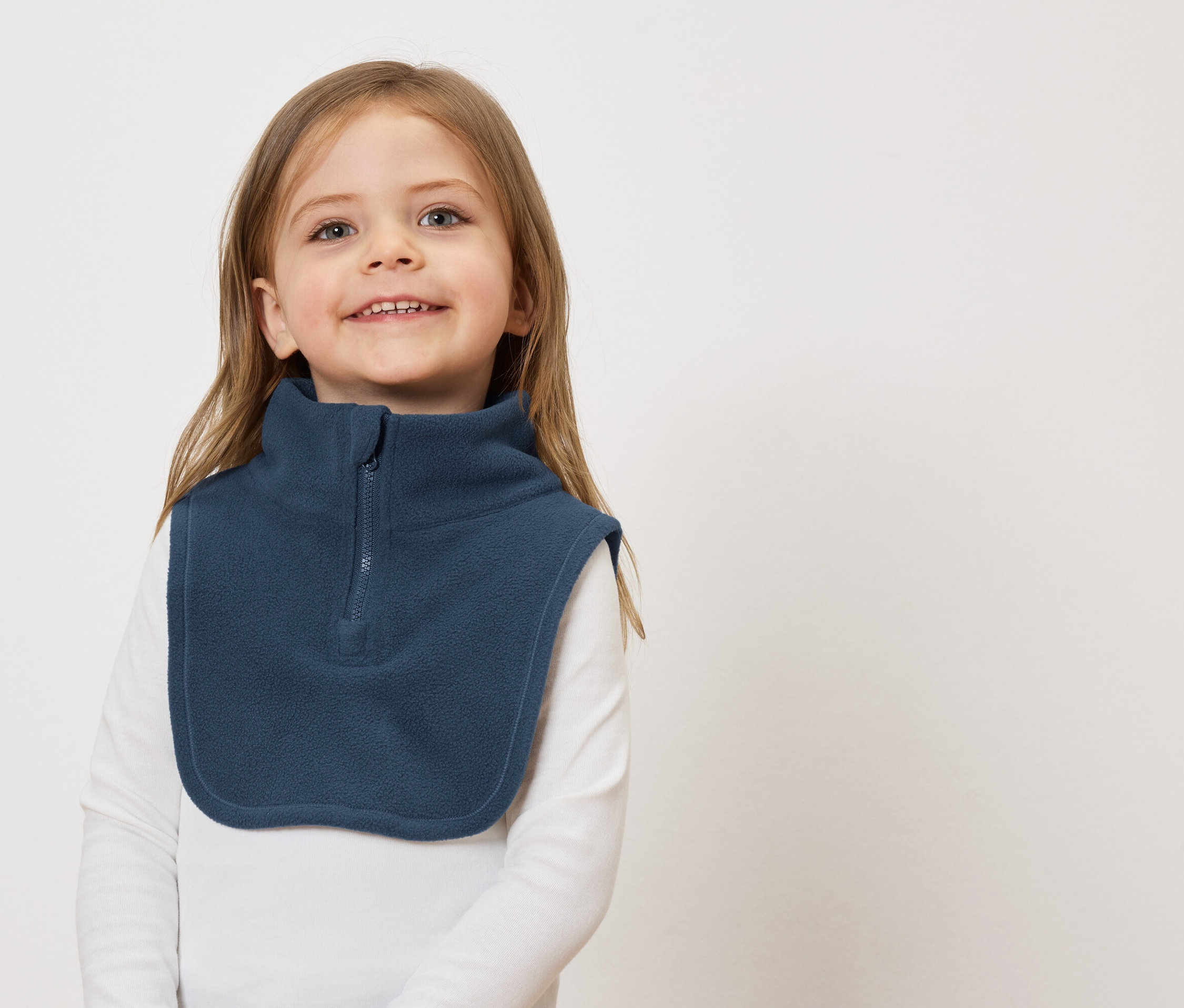 Usmievavé dievča s hnedými vlasmi a modrým flísovým nákrčníkom na bielom pozadí.