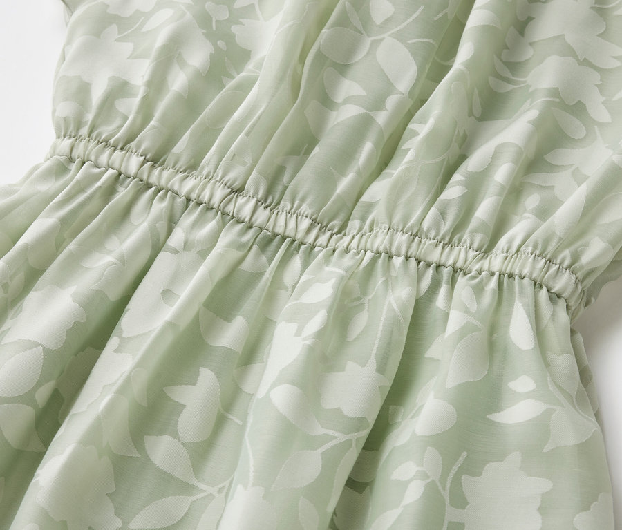 Detail detských šiat s listovou potlačou a elastickým pásom.