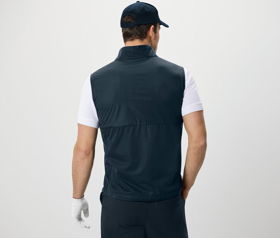 Muž chrbtom ku kamere má na sebe softshellovú vestu, tričko a šiltovku.