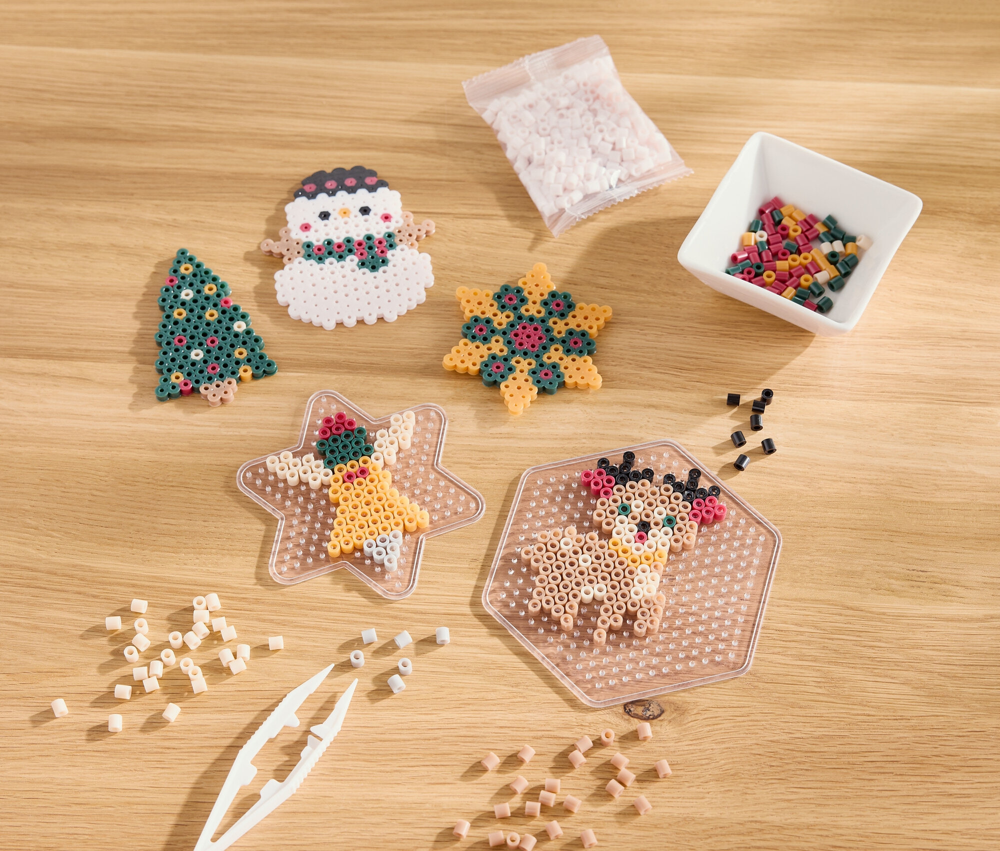 Na drevenom stole ležia vianočné ozdoby z korálok, vrátane stromčeka, snehuliaka, hviezdy a soba.