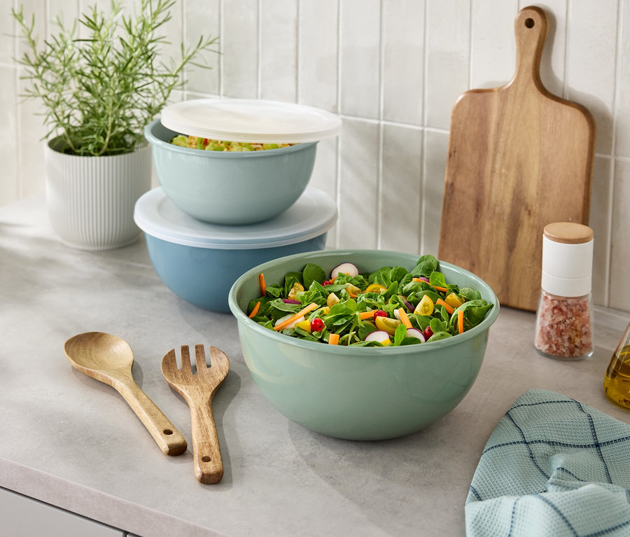 Na kuchynskej linke je misa so šalátom, drevený príbor, soľnička, fľaša oleja, doska na krájanie a rastlina v kvetináči.