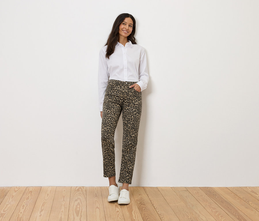Žena v bielej košeli a leopardích nohaviciach stojí pred bielou stenou.