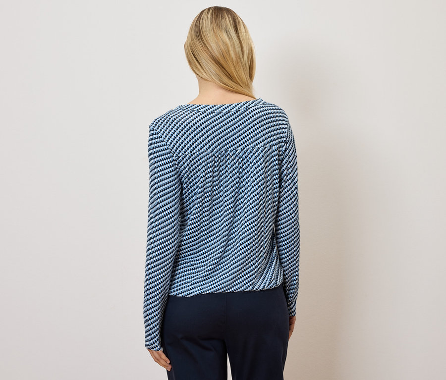 Pohľad zozadu na ženu s blond vlasmi, ktorá má na sebe modro-biele pruhované tričko a tmavomodré nohavice.