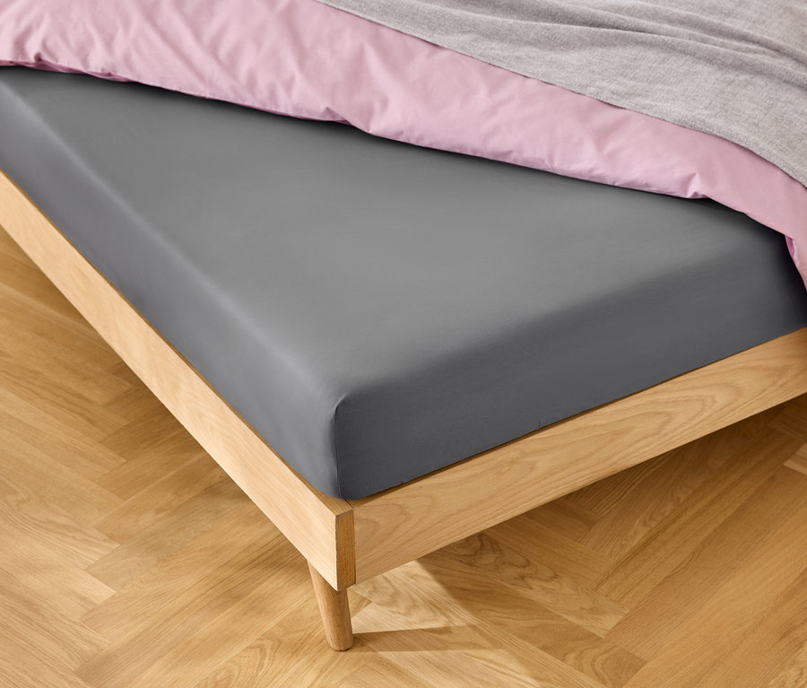 Posteľ so sivou plachtou, ružovým obliečkom a sivou dekou.