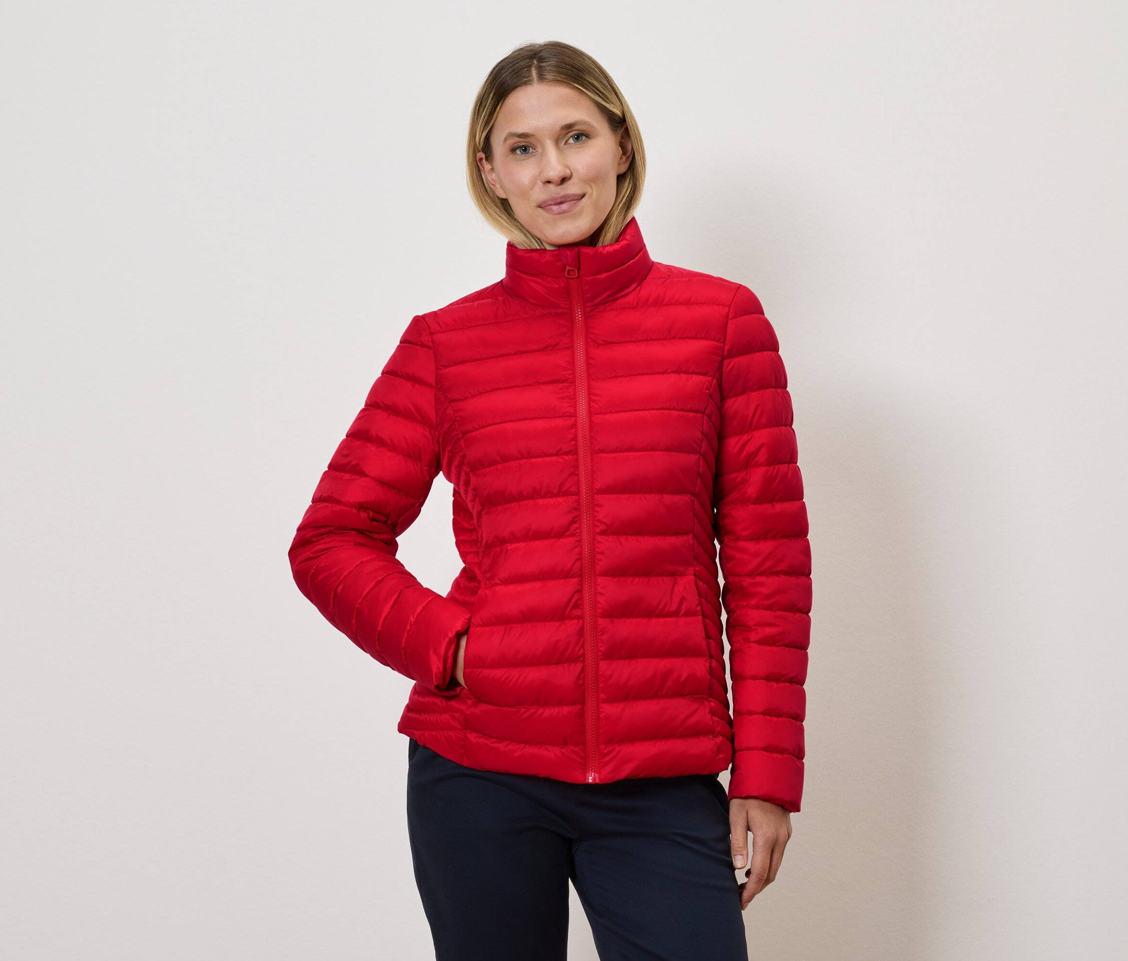 Žena pózuje v červenej prešívanej bunde.