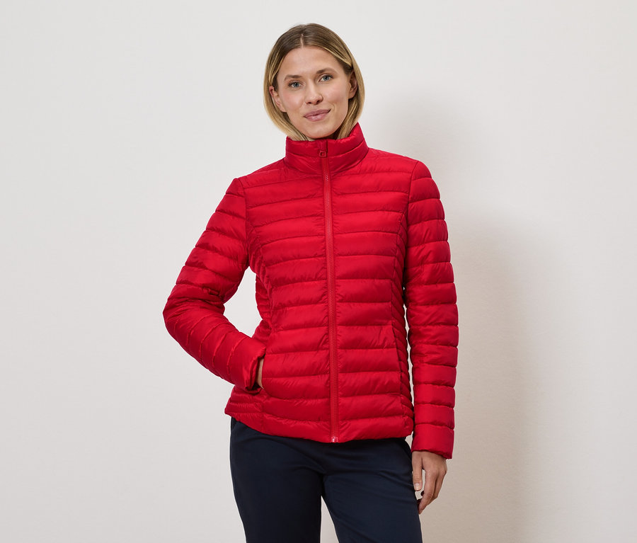 Žena pózuje v červenej prešívanej bunde.