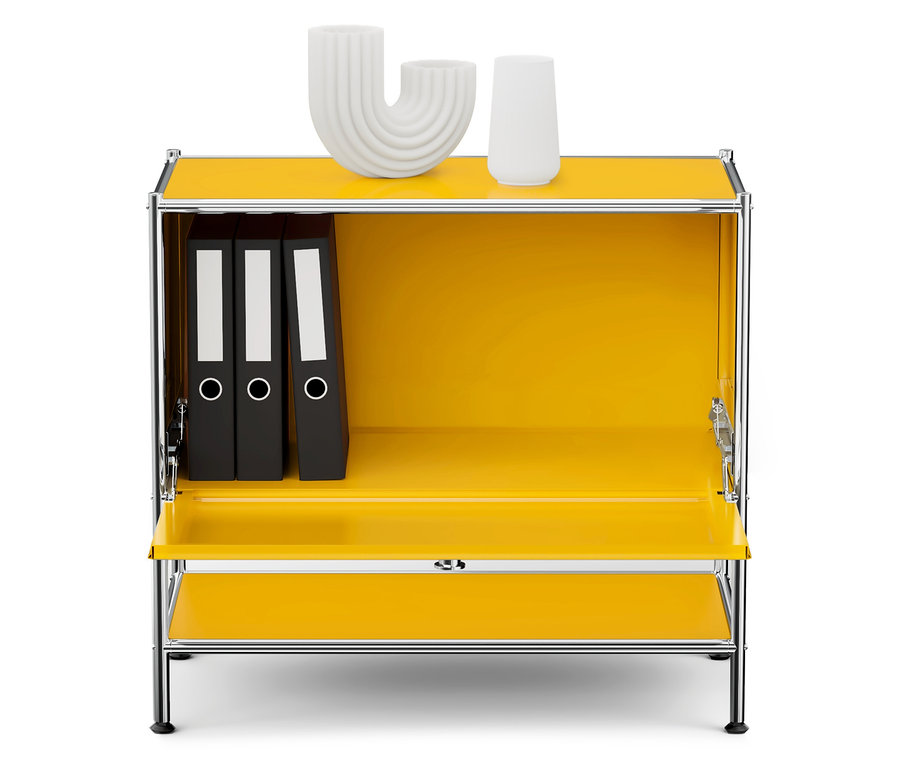 Žltá skrinka s chrómovaným rámom, vnútri sú tri čierne zakladače a na hornej doske dve biele dekorácie.