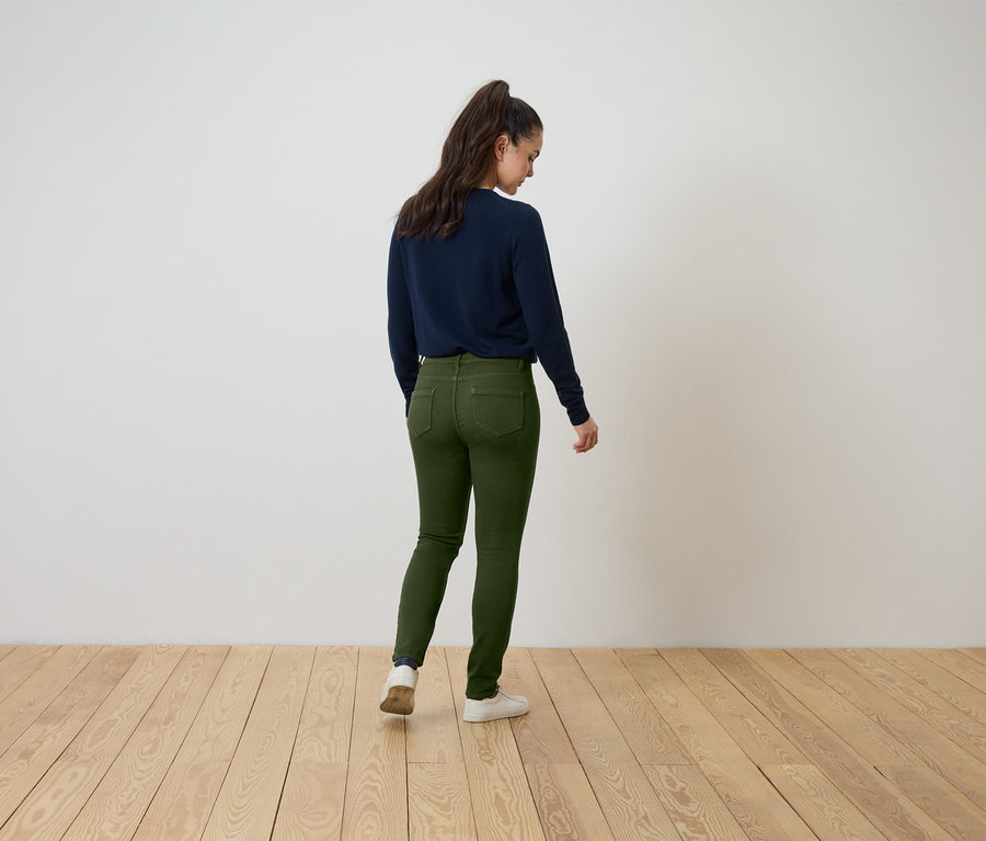 Žena stojí chrbtom, má na sebe tmavomodrý sveter a zelené džínsy.