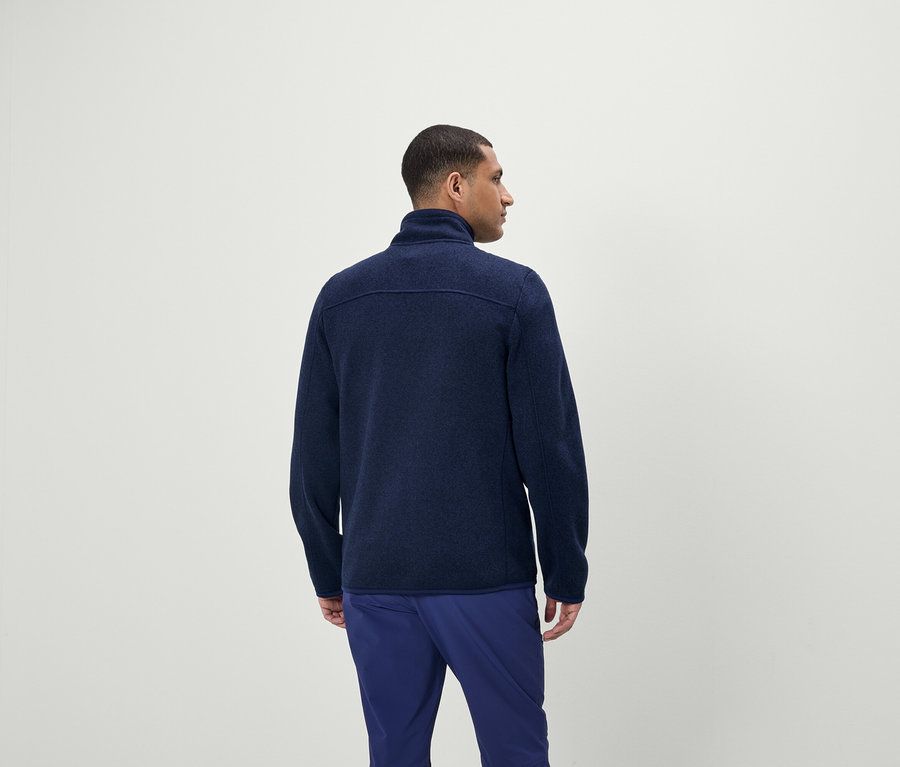 Muž má na sebe modrý sveter na zips a modré nohavice.