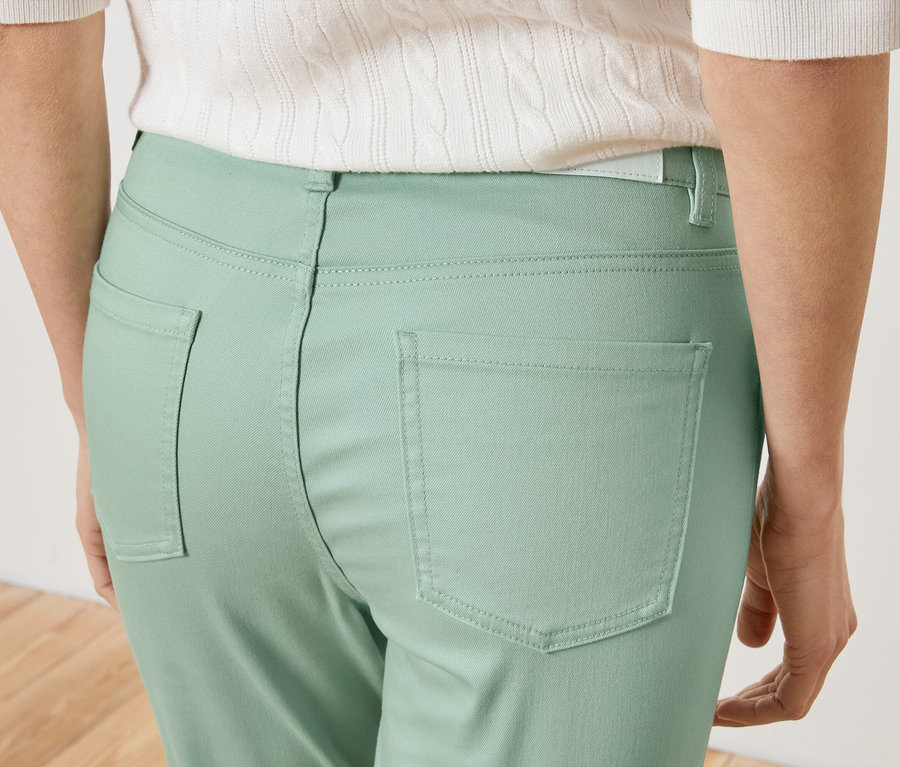 Detailný záber na zadnú časť ženy v svetlozelených nohaviciach a bielom tope.