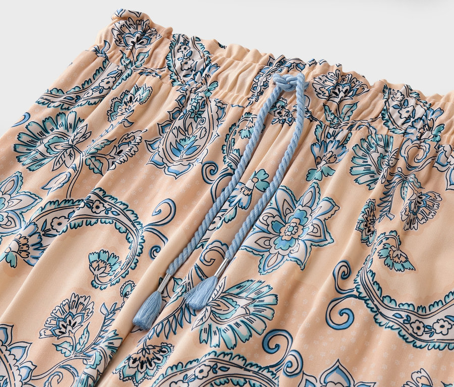 Detailný záber broskyňových nohavíc s modrým kvetinovým vzorom a šnúrkou.