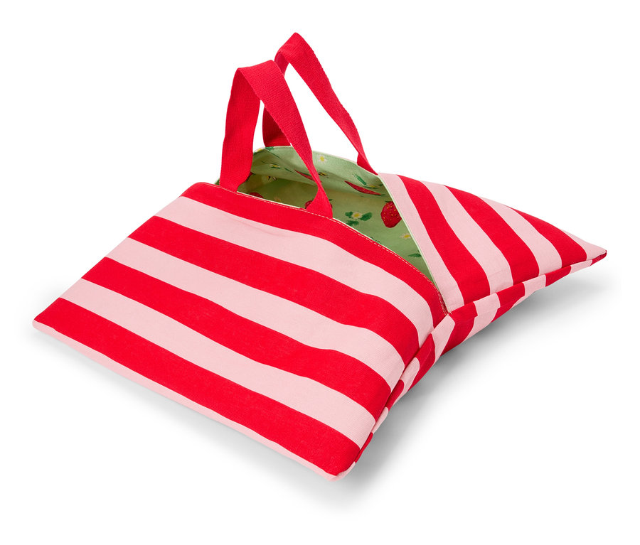 Červeno-biela pruhovaná taška s červenými rúčkami a zelenou podšívkou s jahodovým vzorom leží na bielom povrchu.