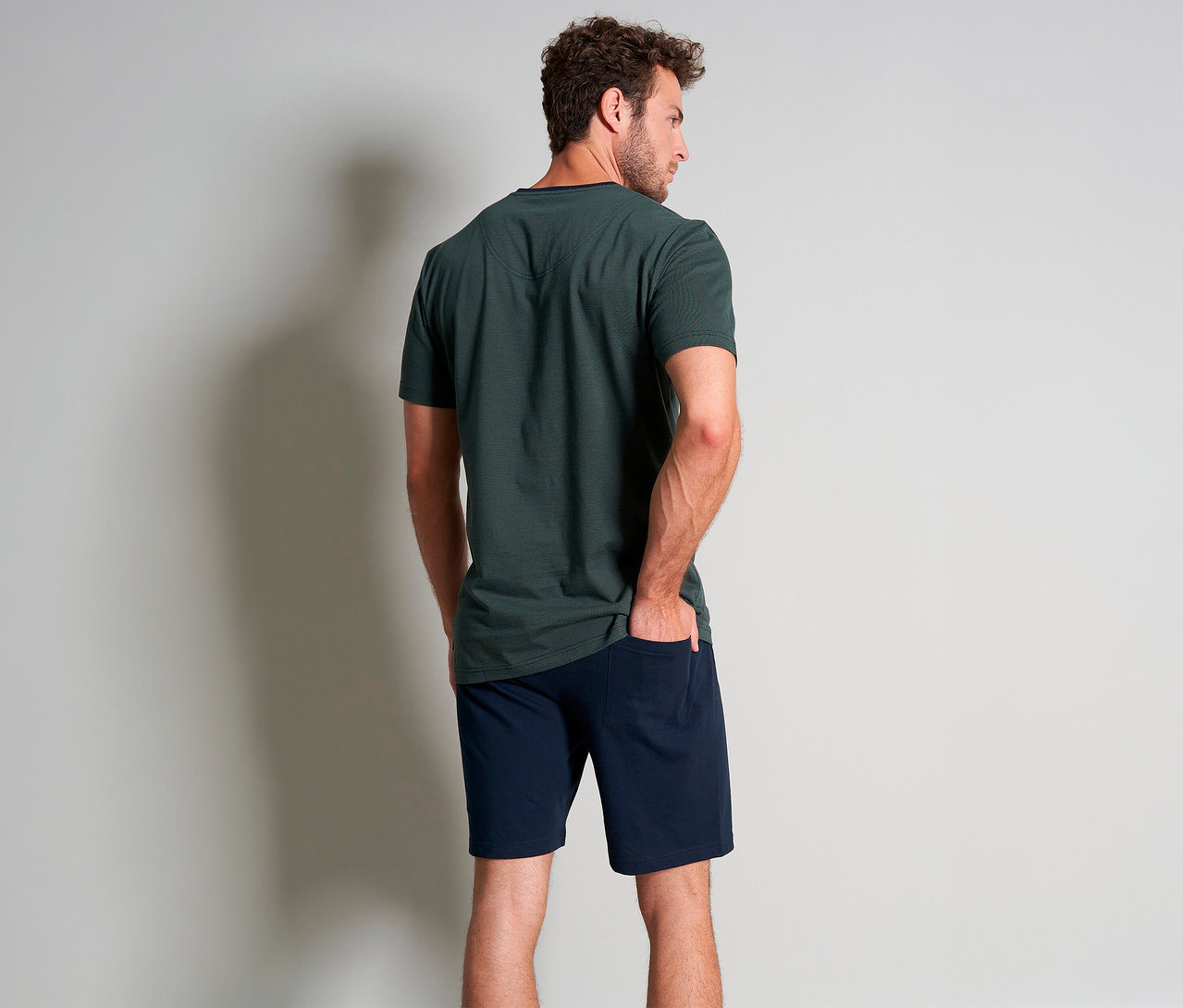 Muž zozadu v zelenom krátkom pyžamovom sete Tom Tailor »Nevada« s rukou vo vrecku.