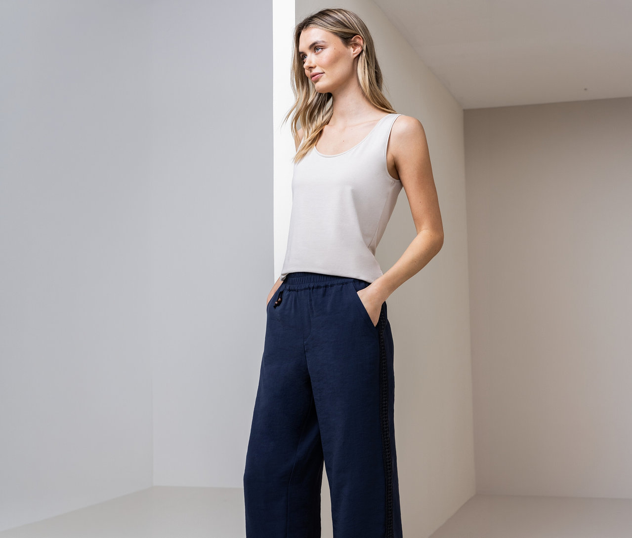 Žena s topom Street One Basic a modrými nohavicami s rukami vo vreckách pred stenou.