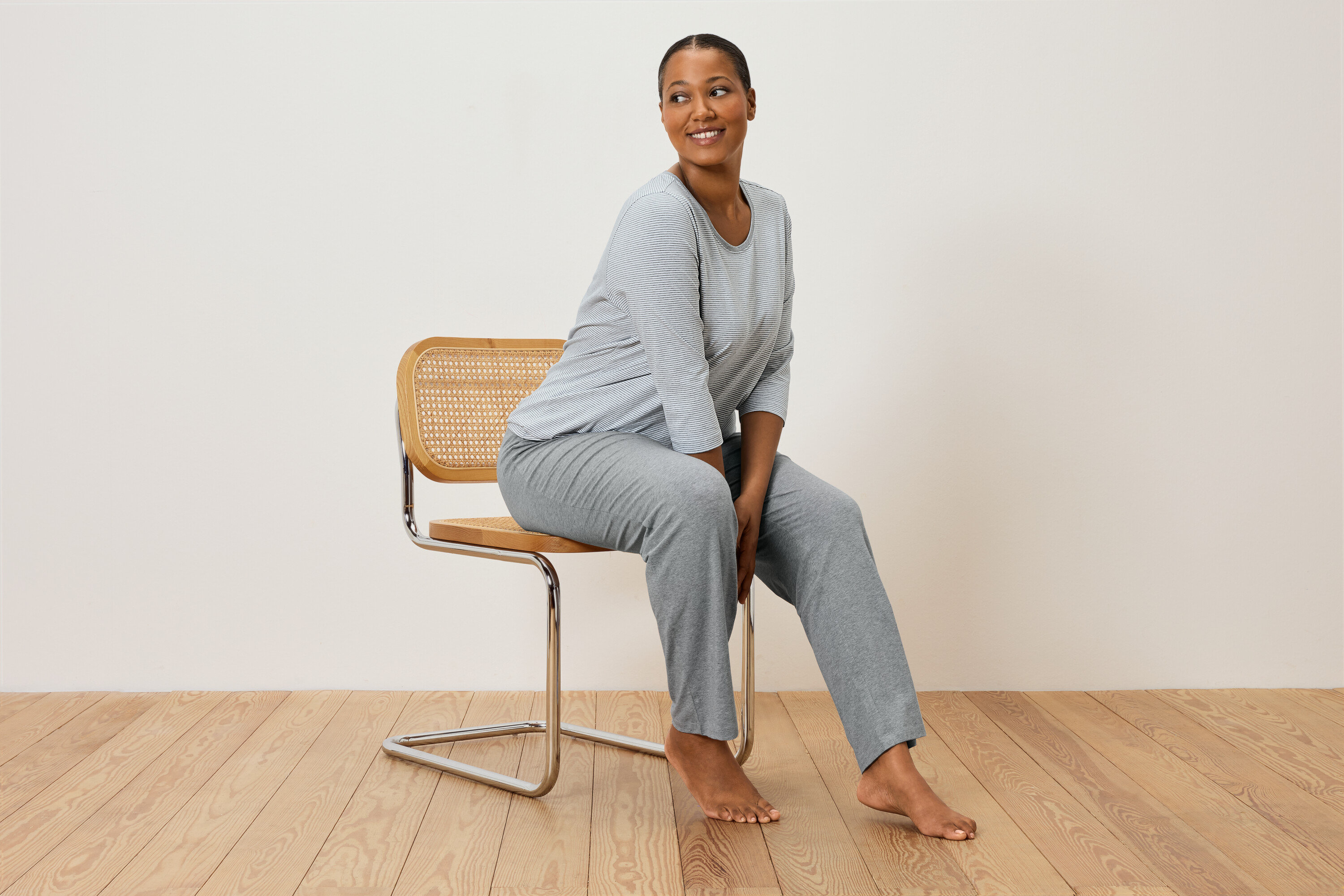 Žena sedí na stoličke v sivom pruhovanom pyžame.