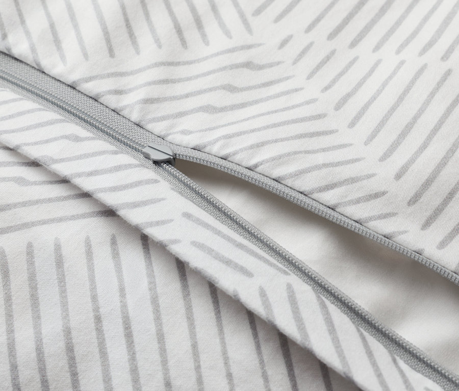 Detailný záber na čiastočne otvorenú obliečku na prikrývku so zipsom a sivým prúžkovaným vzorom na bielom pozadí.