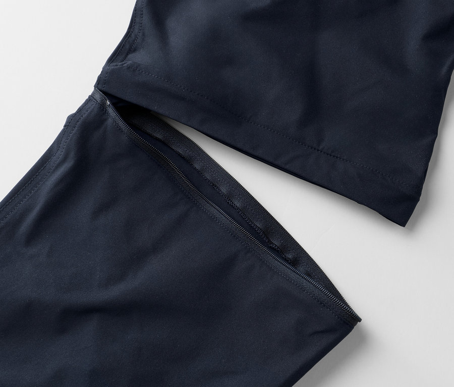 Detailný záber na námornícke modré nohavice s odhaleným zipsom na bielom pozadí.