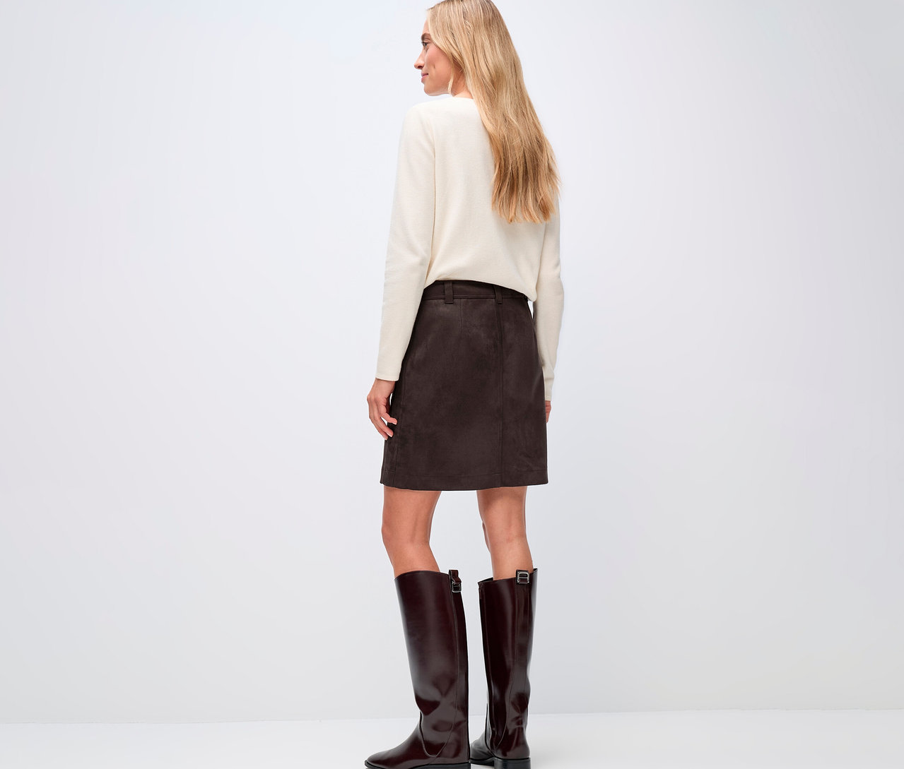 Žena zozadu, má na sebe krémový sveter a hnedú velúrovú sukňu Street One a k tomu hnedé čižmy.