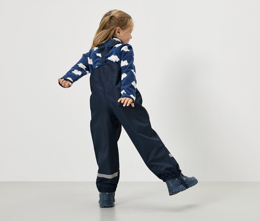 Dievča v námorníckych modrých dažďových nohaviciach a modrom svetri s obláčikovým vzorom, pohľad zozadu.