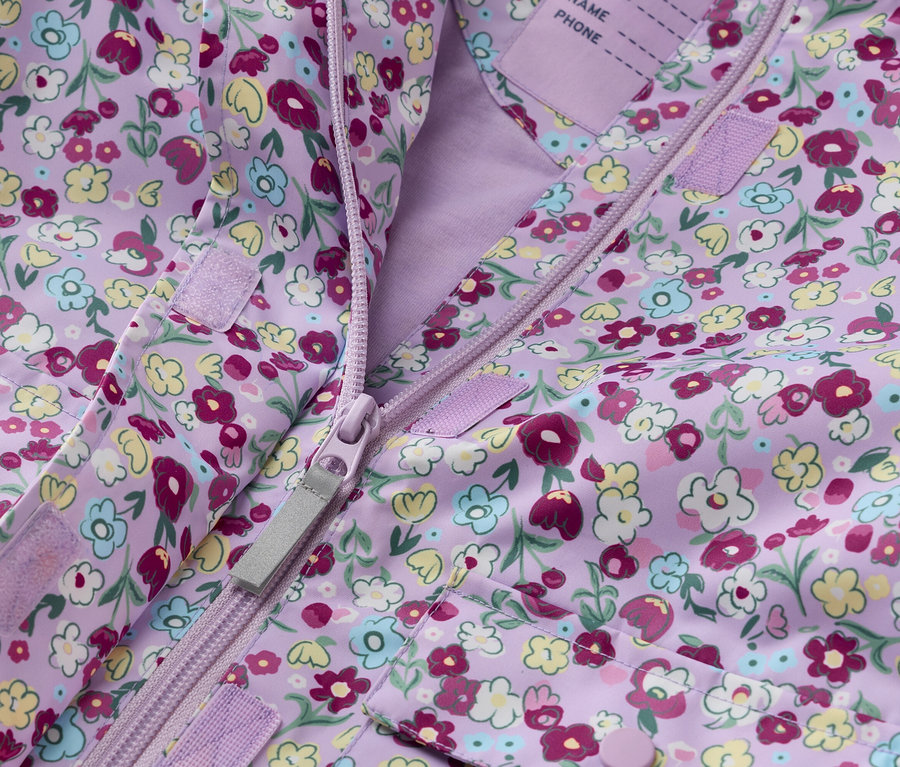 Detail fialovej detskej bundy s kvetinovou potlačou, rozopnutej na zips.