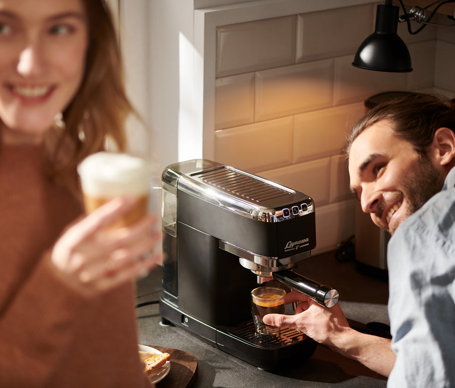 Muž pripravuje espresso na pákovom kávovare Lapressa čierny, žena drží latte.