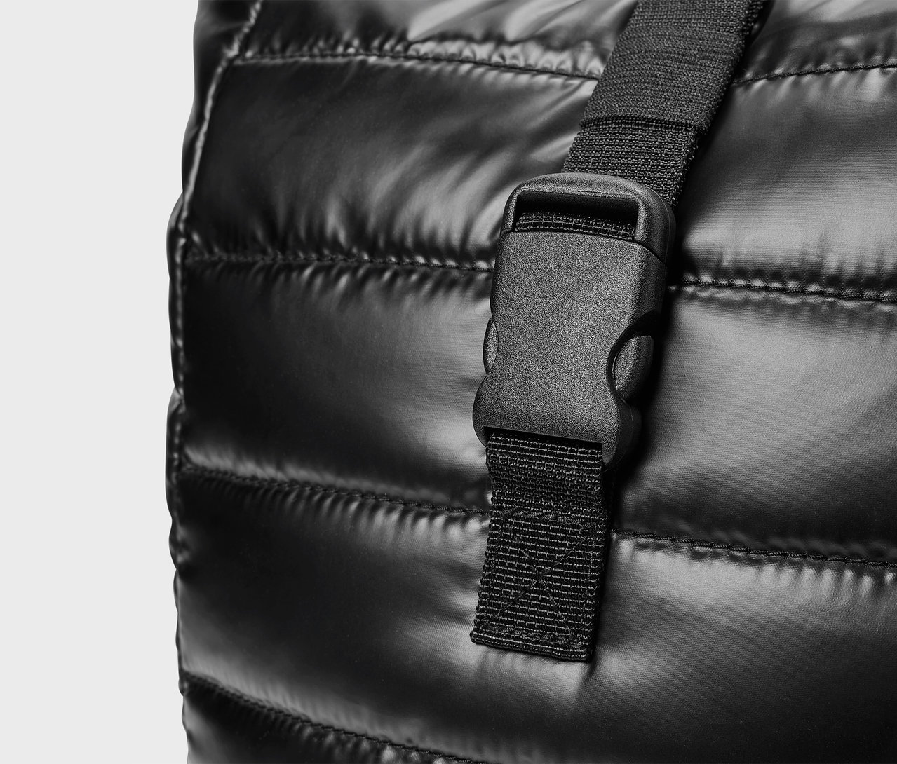 Detail čiernej prešívanej tašky s plastovou sponou.