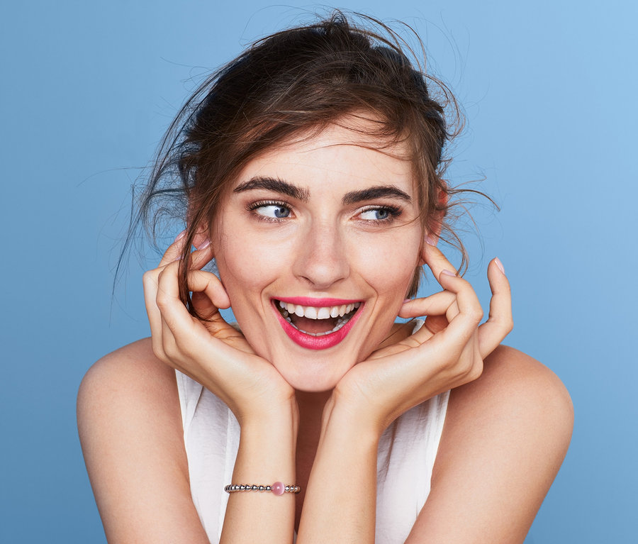 Usmievajúca sa žena na svetlomodrom pozadí má na sebe náramok.