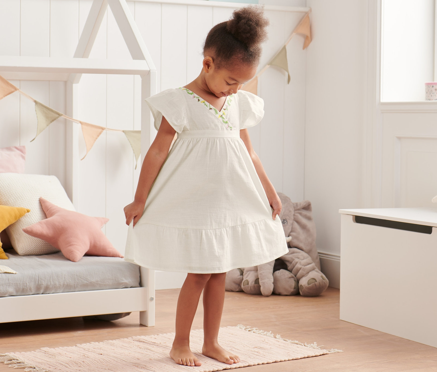Dievča stojí na koberci a má na sebe tkané šaty z biobavlny.