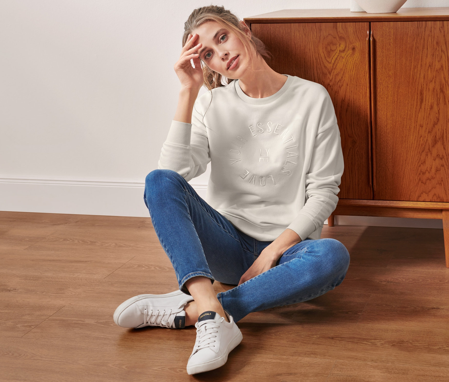 Žena sedí na podlahe a má na sebe krémovú mikinu.