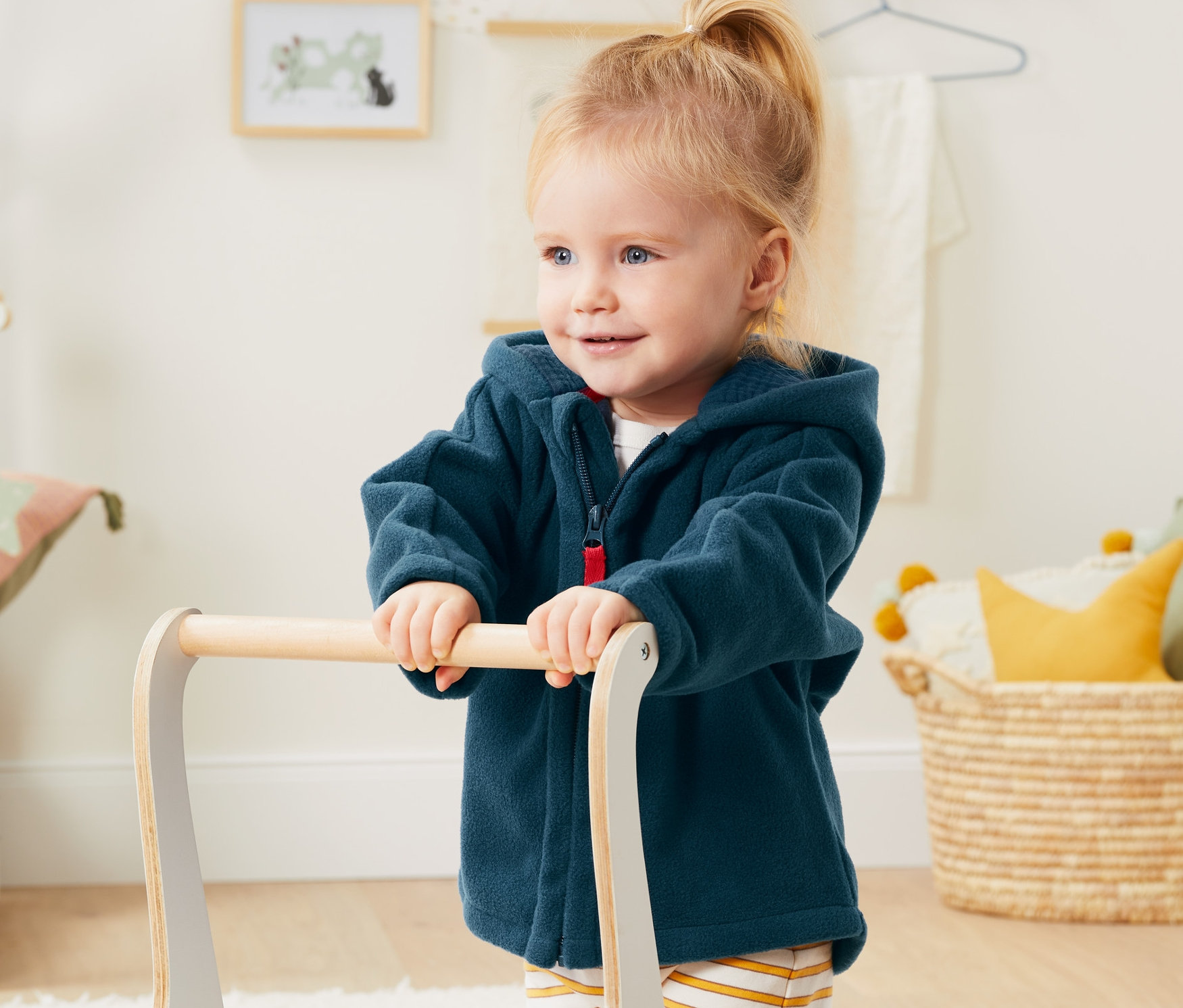 Batoľa tlačí chodítko a má na sebe flísovú bundu s recyklovaného materiálu.