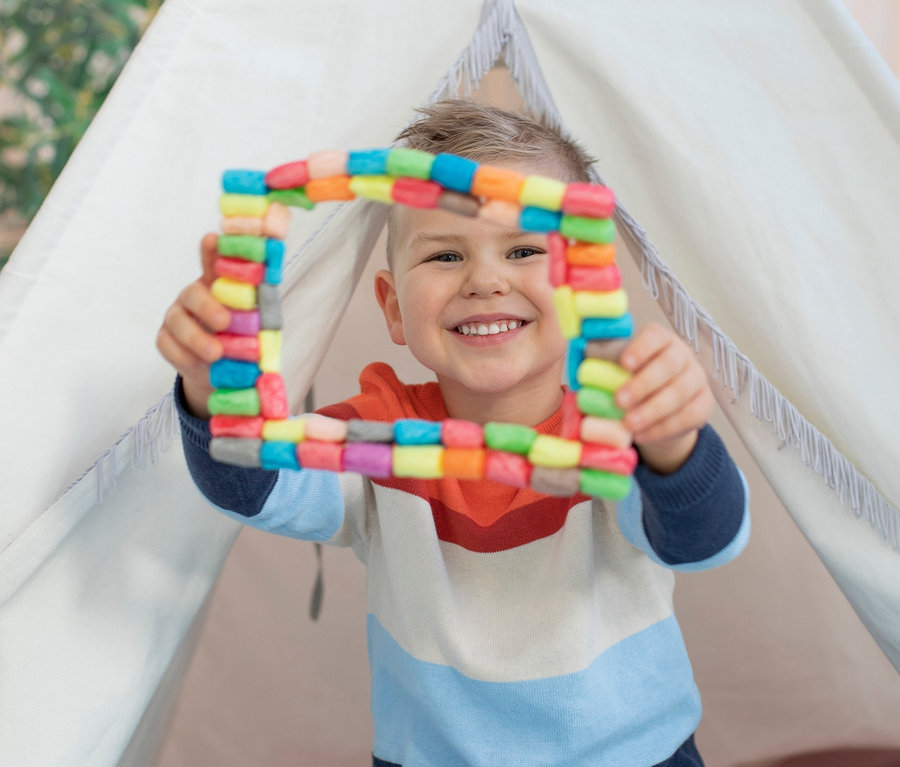 Chlapec sedí v teepee a drží v rukách farebný štvorec zo súpravy PlayMais®.