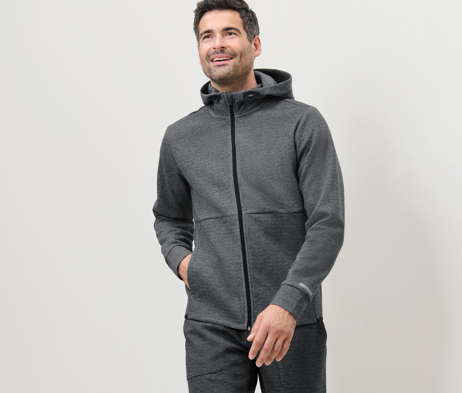 Muž má na sebe sivú funkčnú teplákovú mikinu.
