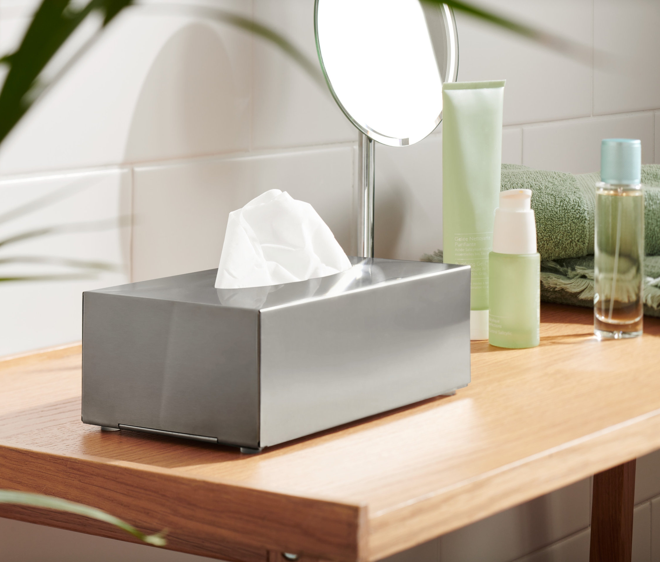 Kovový zásobník na vreckovky s bielymi vreckovkami na drevenej polici.