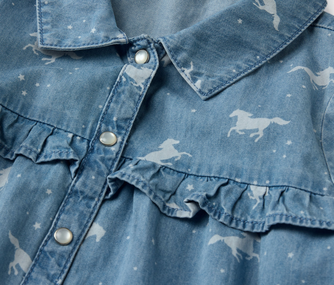 Detail detských džínsových šiat s potlačou koní a volánmi.