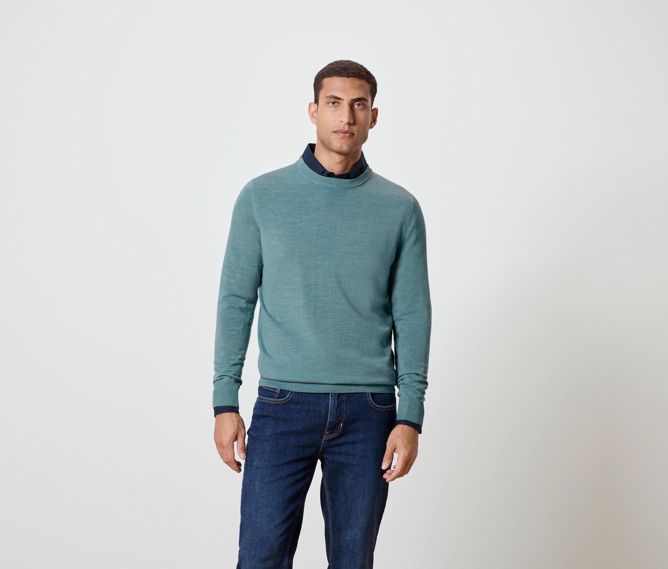 Muž pózuje v modrom svetri a džínsoch.