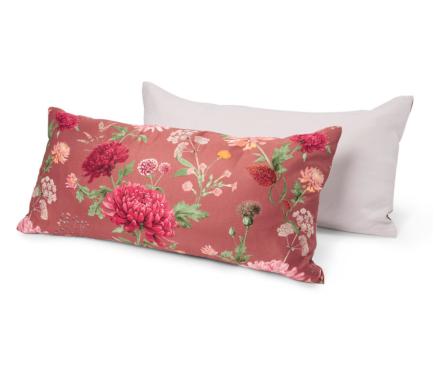 Dva vankúše ležia na sebe. Spodný vankúš má kvetinový vzor s červenými a ružovými kvetmi na červenom pozadí. Vrchný vankúš je biely.