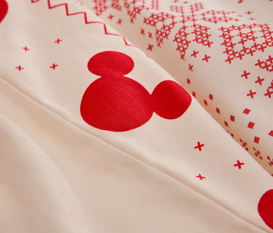 Detail bielej posteľnej bielizne s červeným vzorom Mickey Mouse a vianočnými motívmi.