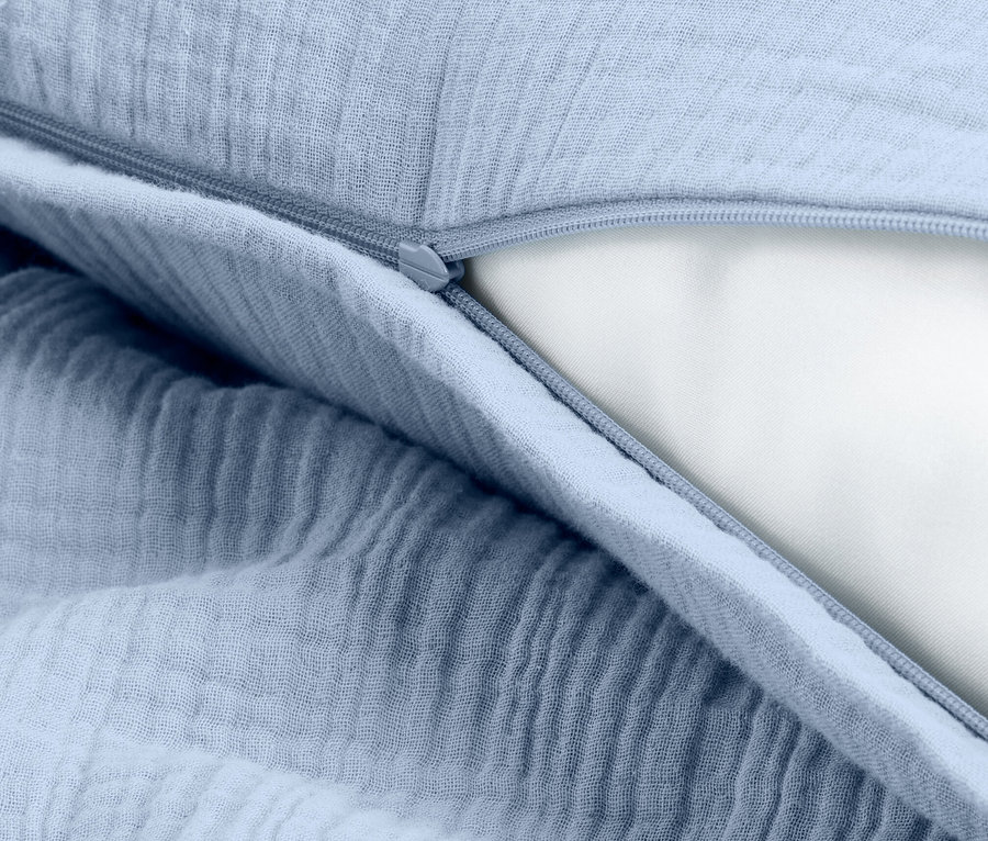 Detail svetlomodrej obliečky na vankúš so zipsom, odhaľujúci bielu výplň vankúša.