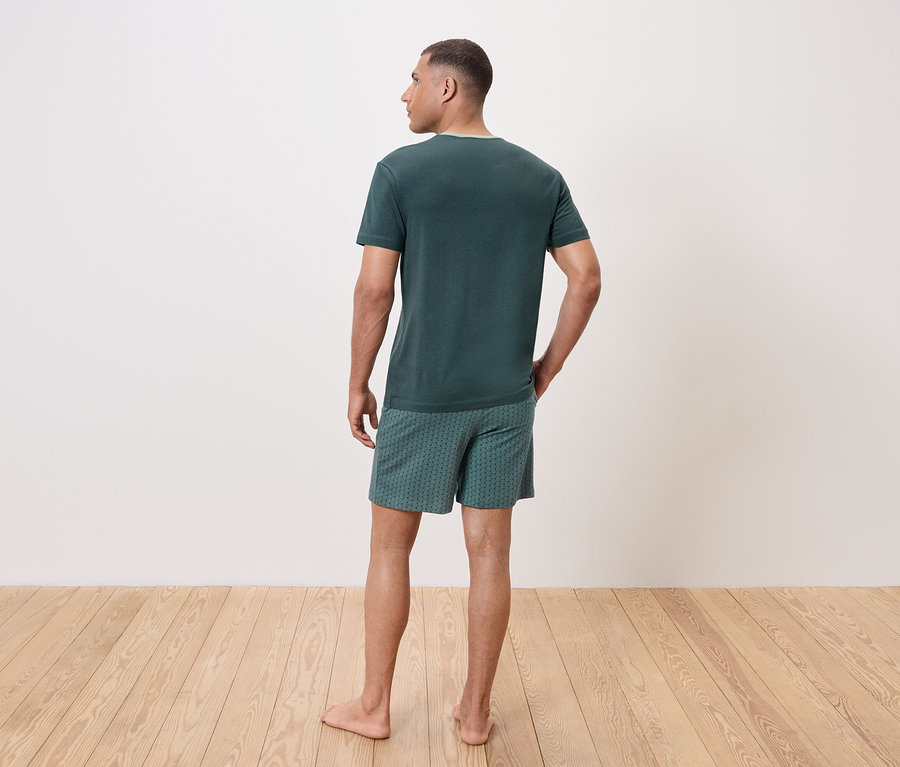 Muž chrbtom k fotoaparátu má na sebe zelené tričko a vzorované šortky.