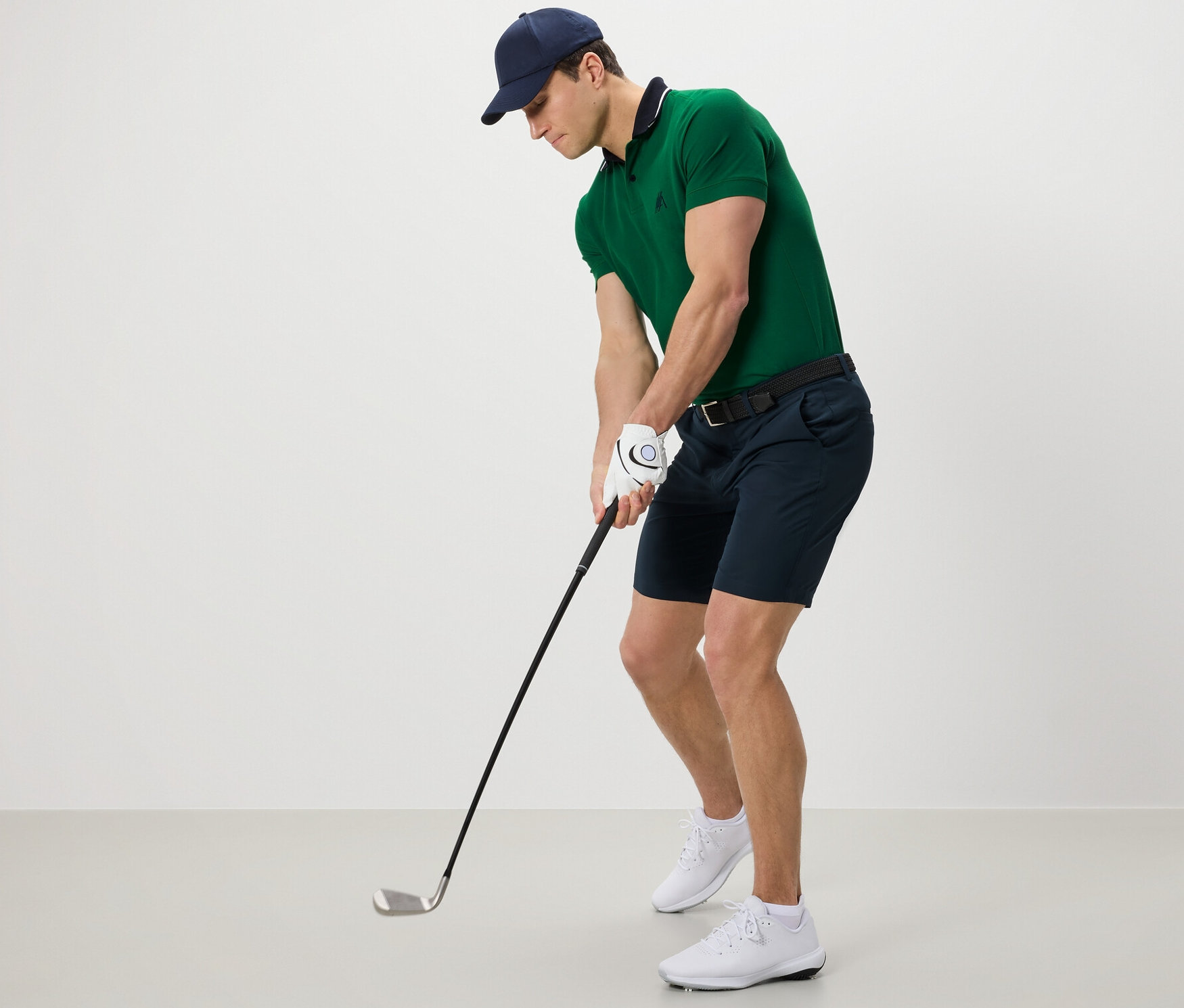 Muž v zelenom polo tričku a funkčných šortkách hrá golf.