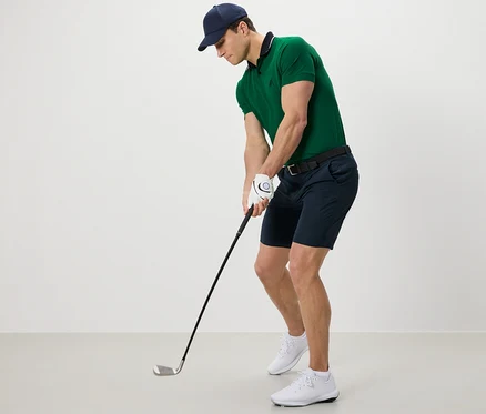 Muž v zelenom polo tričku a funkčných šortkách hrá golf.
