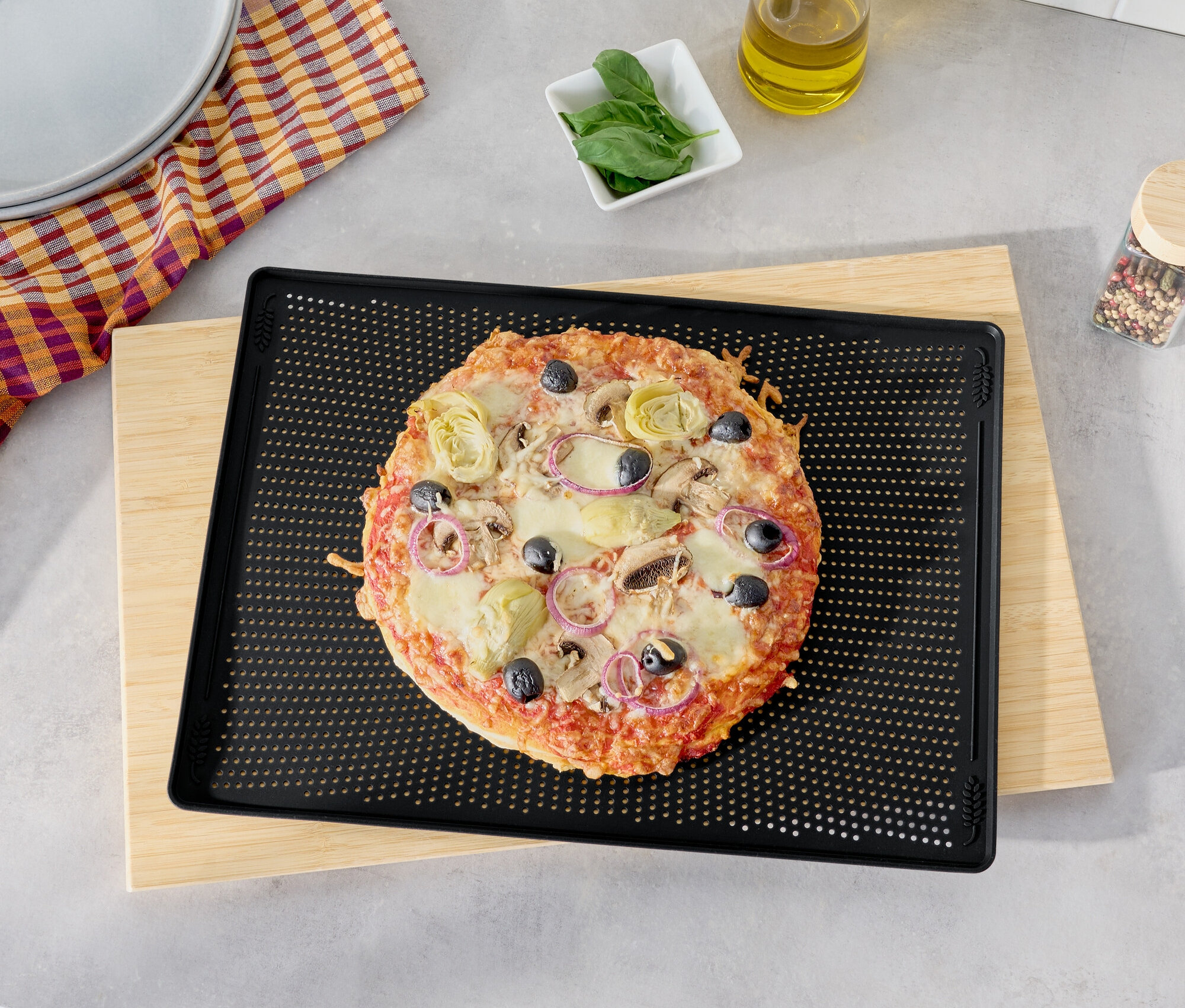 Pizza s olivami, artičokmi a červenou cibuľou na čiernom plechu na pečenie na drevenej doske na krájanie.