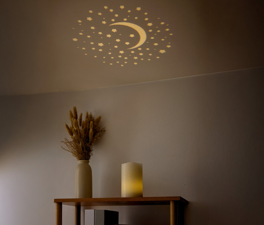 Na strope sú viditeľné hviezdy a polmesiac. Na poličke je váza so sušenými kvetmi a sviečka.