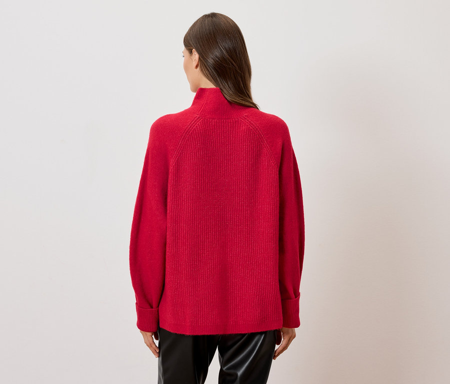 Žena chrbtom k fotoaparátu má na sebe červený rolák a čierne kožené nohavice.