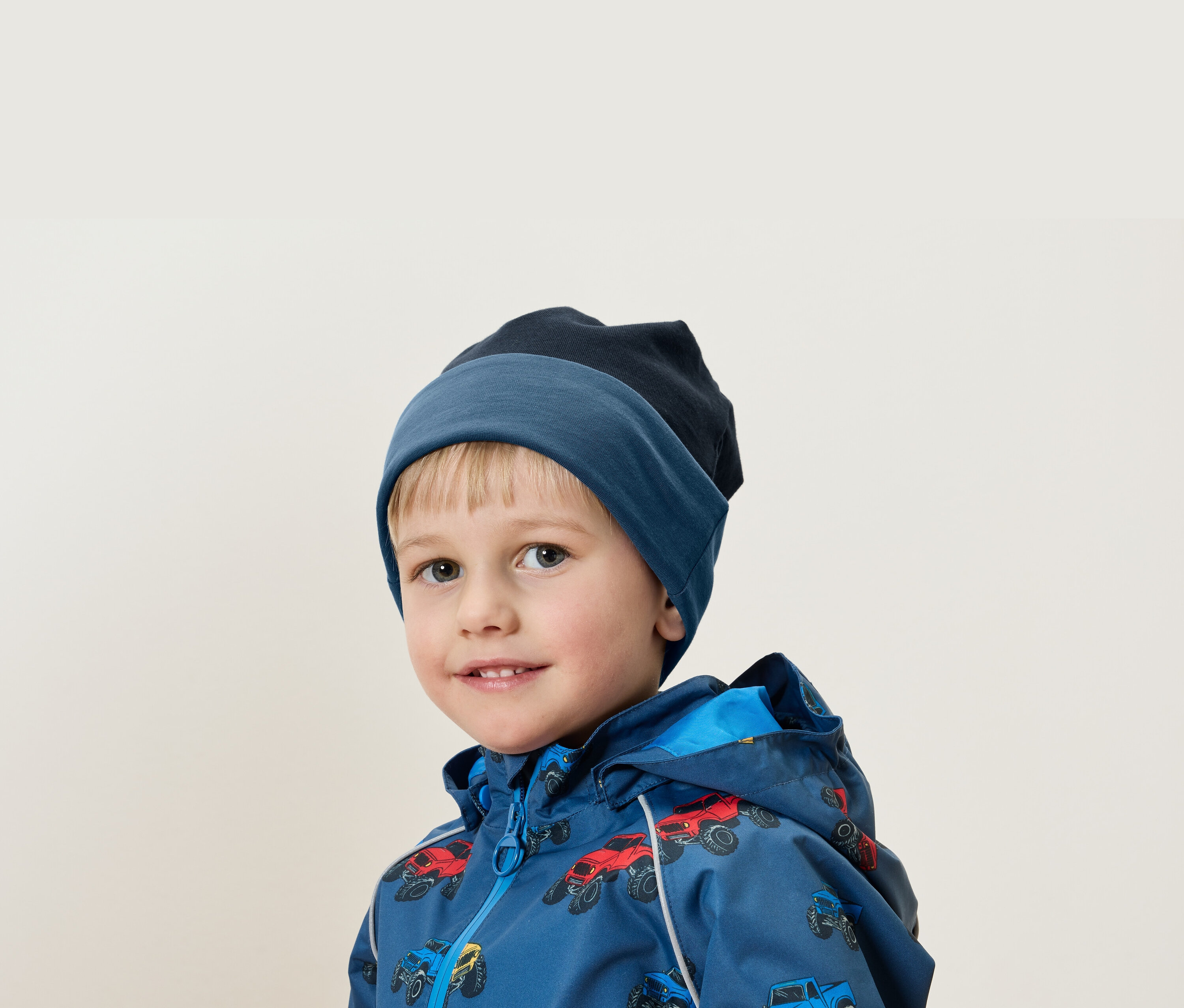 Portrét chlapca s blond vlasmi v modrej čiapke a bunde s potlačou áut.